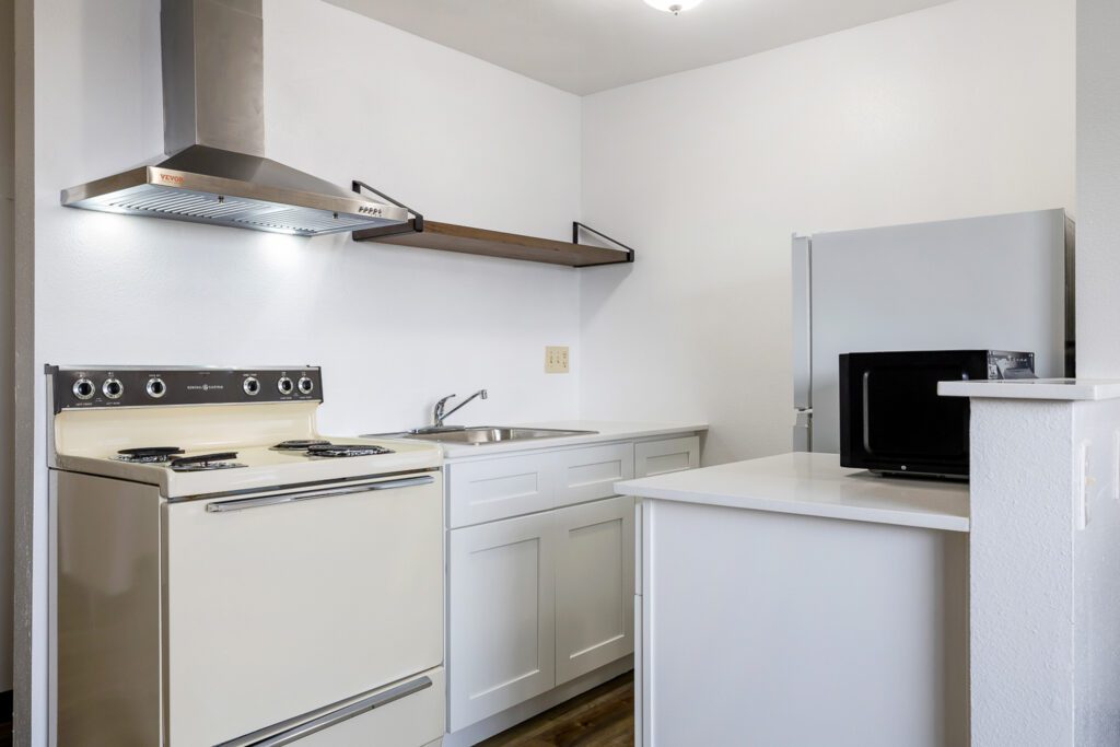 Hotel room kitchen at Kennewick Inn & Suites Tri Cities with stove, sink, refrigerator, and microwave.
